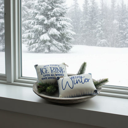 Two decorative mini pillows with text on a wooden plate with pine branches