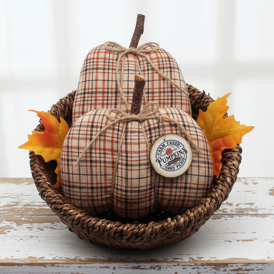 Decorative homespun fabric pumpkins with a tag in a woven basket on a white background