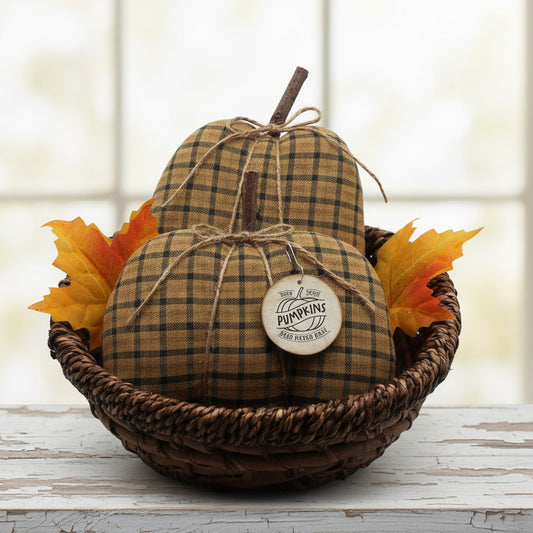 Decorative homespun pumpkins with plaid pattern in a woven basket with fall leaves on a light background