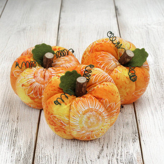 Three decorative pumpkins with sunflower patterns on a wooden surface