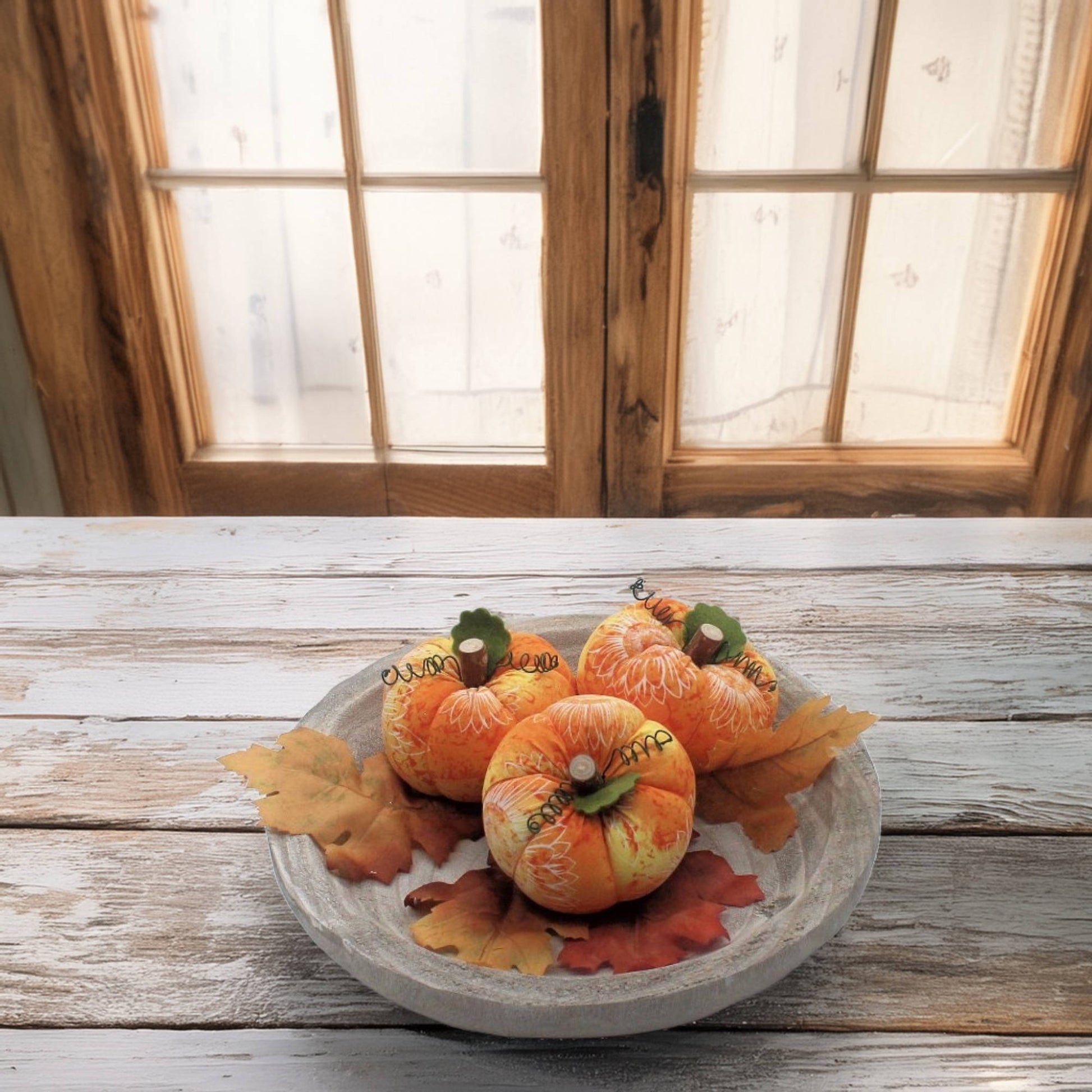 Decorative pumpkins on a wood platter with autumn leaves against a wooden window background