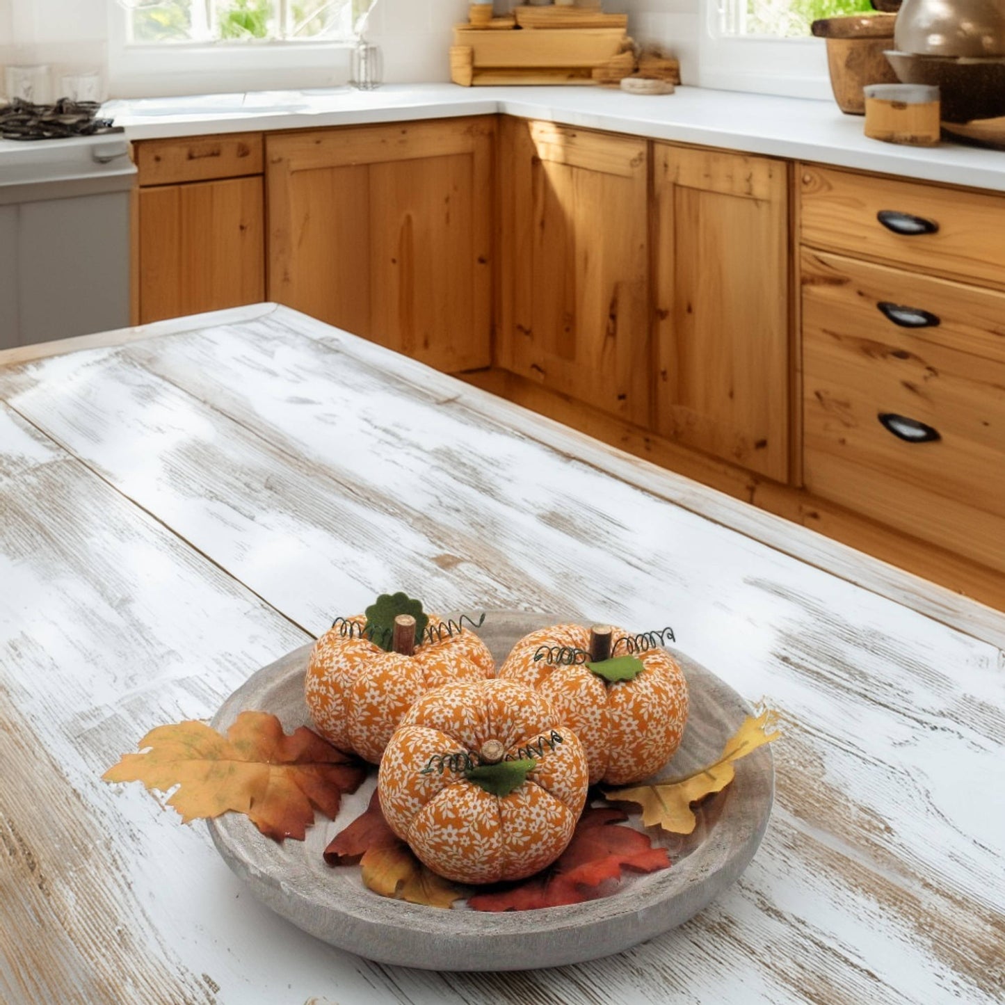 Decorative pumpkins on a wooden tray with fall leaves in a kitchen setting