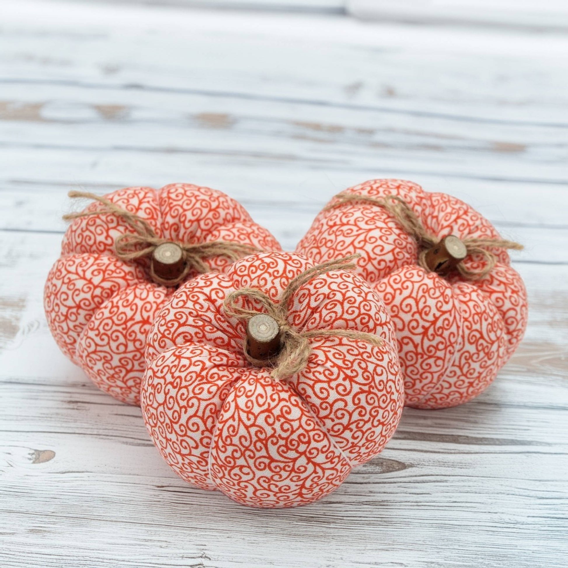 Three decorative fabric pumpkins with orange patterns on a wooden surface
