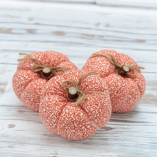 Three decorative fabric pumpkins with orange patterns on a wooden surface