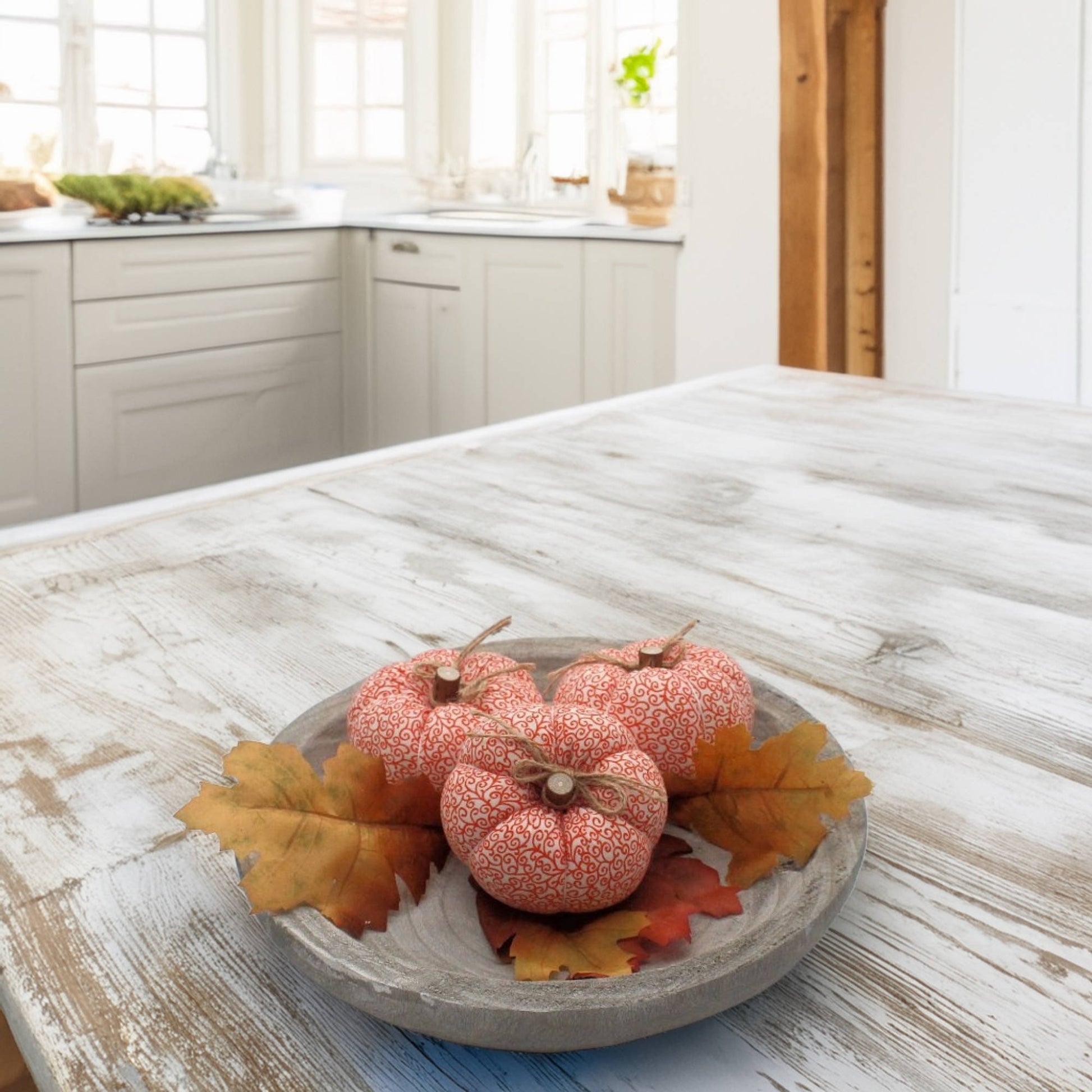 Decorative  fabric pumpkins with leaves on a wooden table in a kitchen.