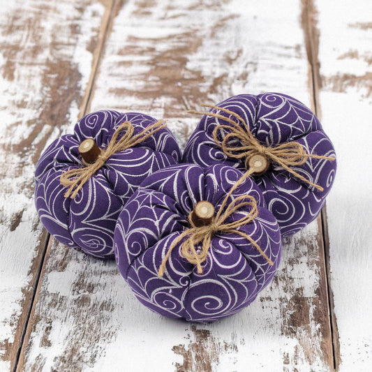 Three purple fabric pumpkins with jute twine bows on a wooden surface
