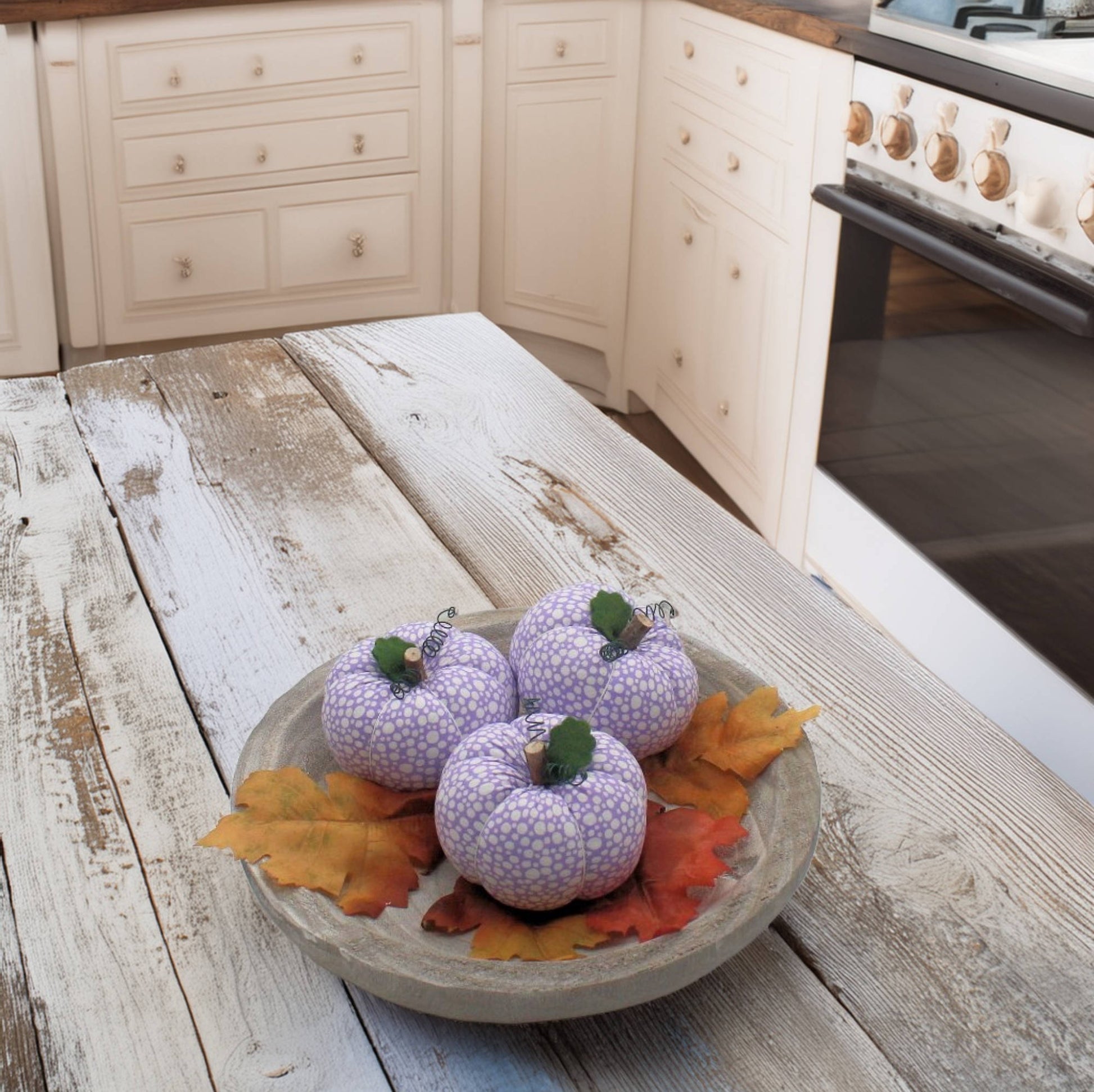 Decorative purple pumpkins with green stems on a wooden surface in a kitchen.