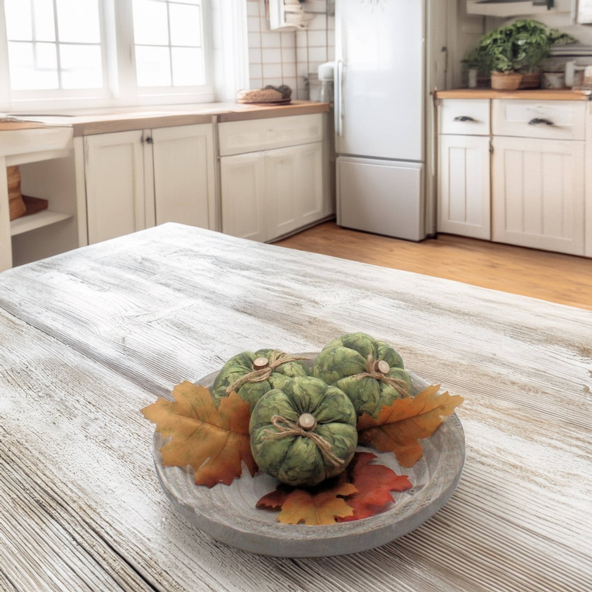 Decorative arrangement of green pumpkins and autumn leaves on a kitchen table.