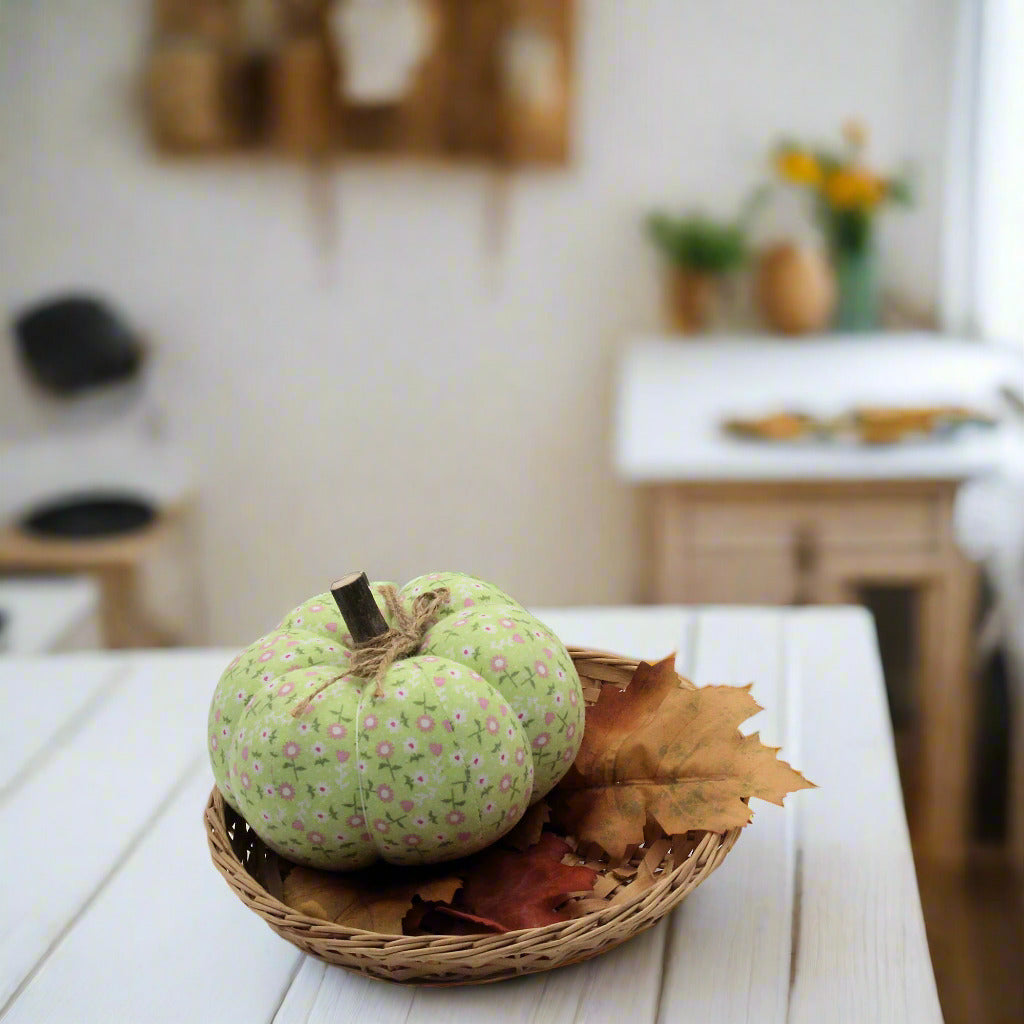 Decorative green pumpkin with floral pattern in a woven basket on a white table.