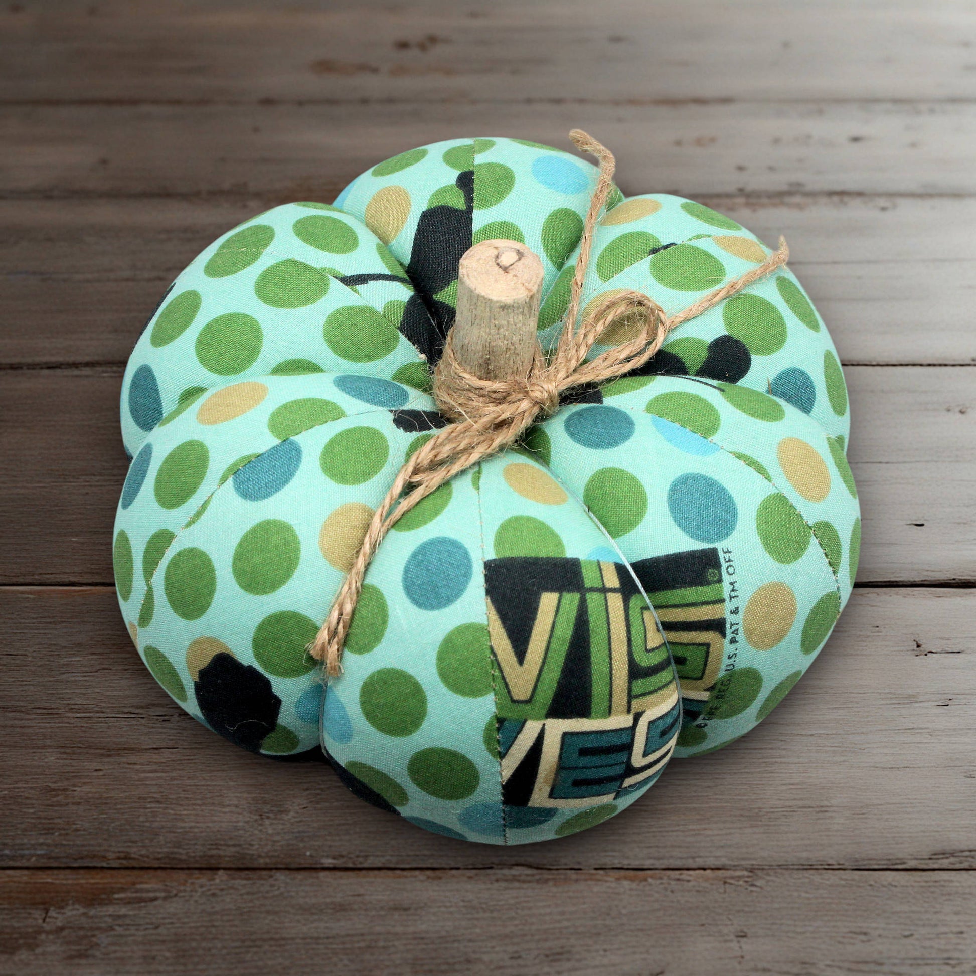 Decorative pumpkin with green and blue polka dot pattern on a wooden surface