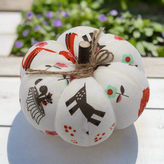 Decorative white pumpkins with colorful designs on a white surface with a blurred green and purple plant background.