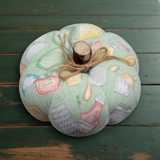 Decorative fabric pumpkin with kitchen-themed design on a wooden surface