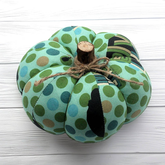 Decorative pumpkin with green and blue polka dot pattern on a white wooden surface