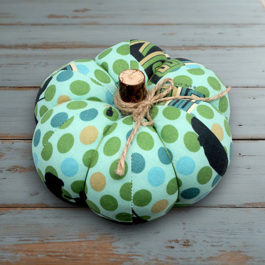 Decorative pumpkin with green and blue polka dot pattern on a white wooden surface