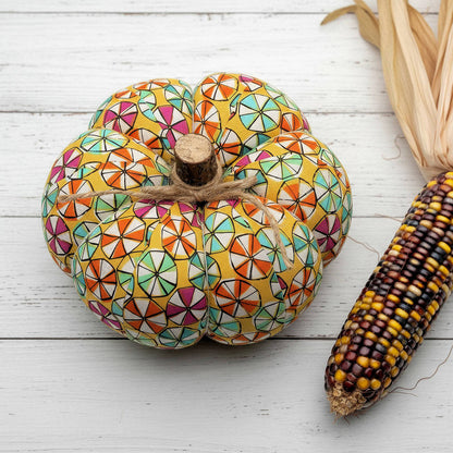 Decorative pumpkin with a colorful candy pattern next to an ear of corn on a wooden surface
