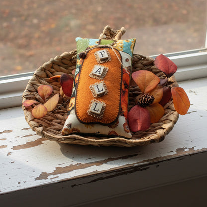 Decorative pillow with 'FALL' text on a woven plate with autumn leaves
