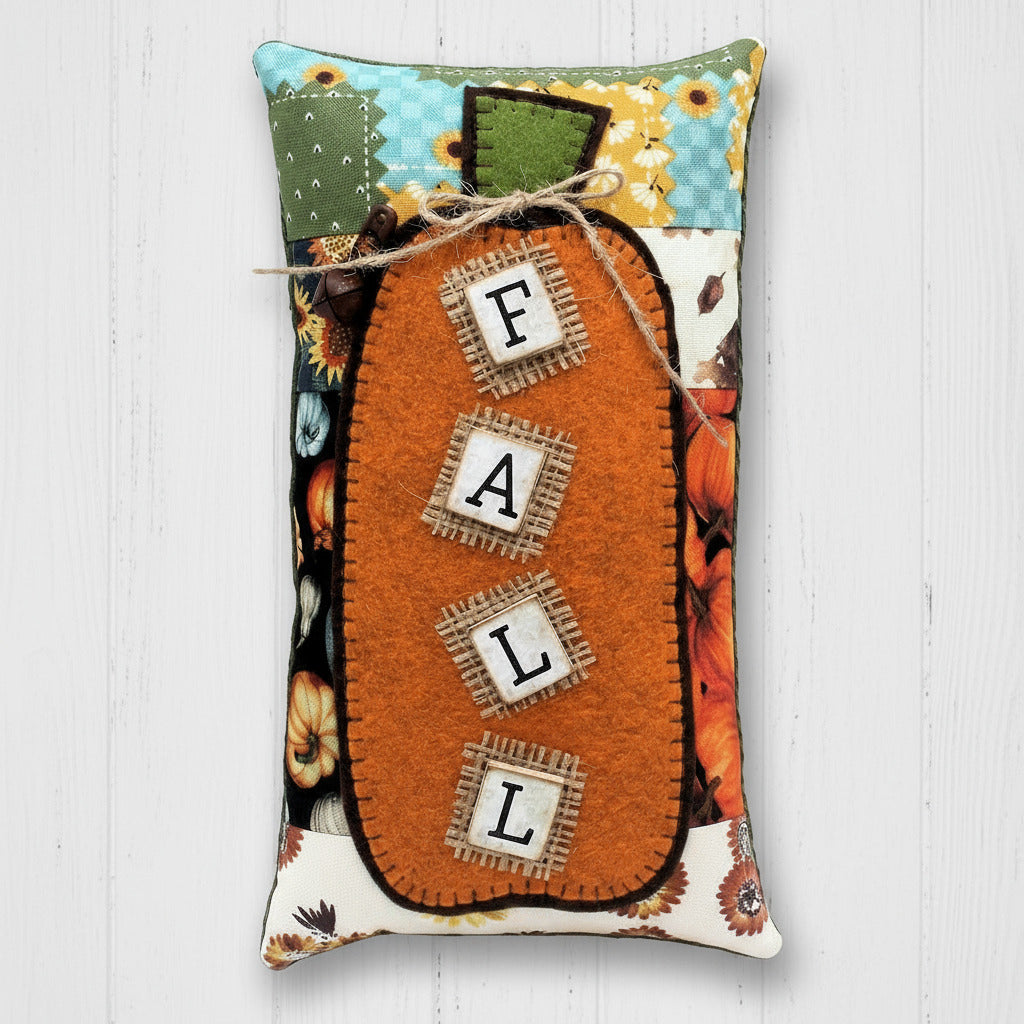 Decorative pillow with 'Fall' text and pumpkin design on a wooden surface