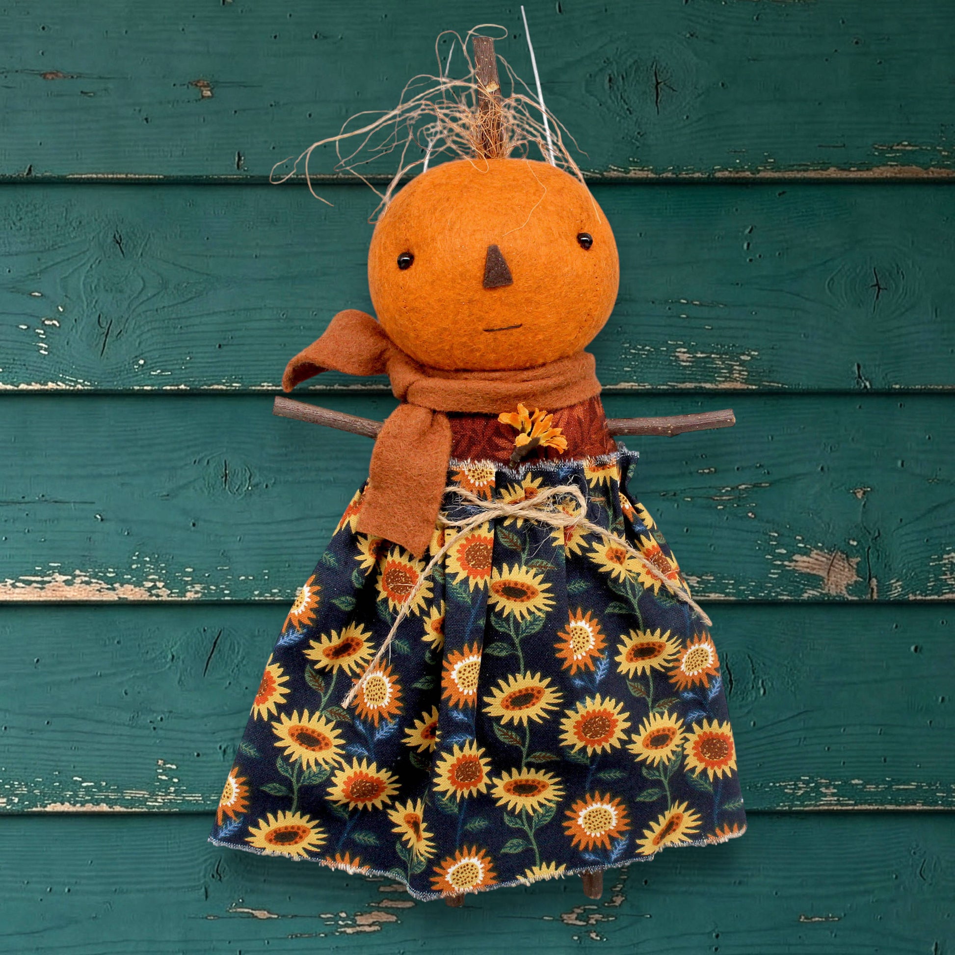 Pumpkin character doll with a sunflower dress against a teal wooden background