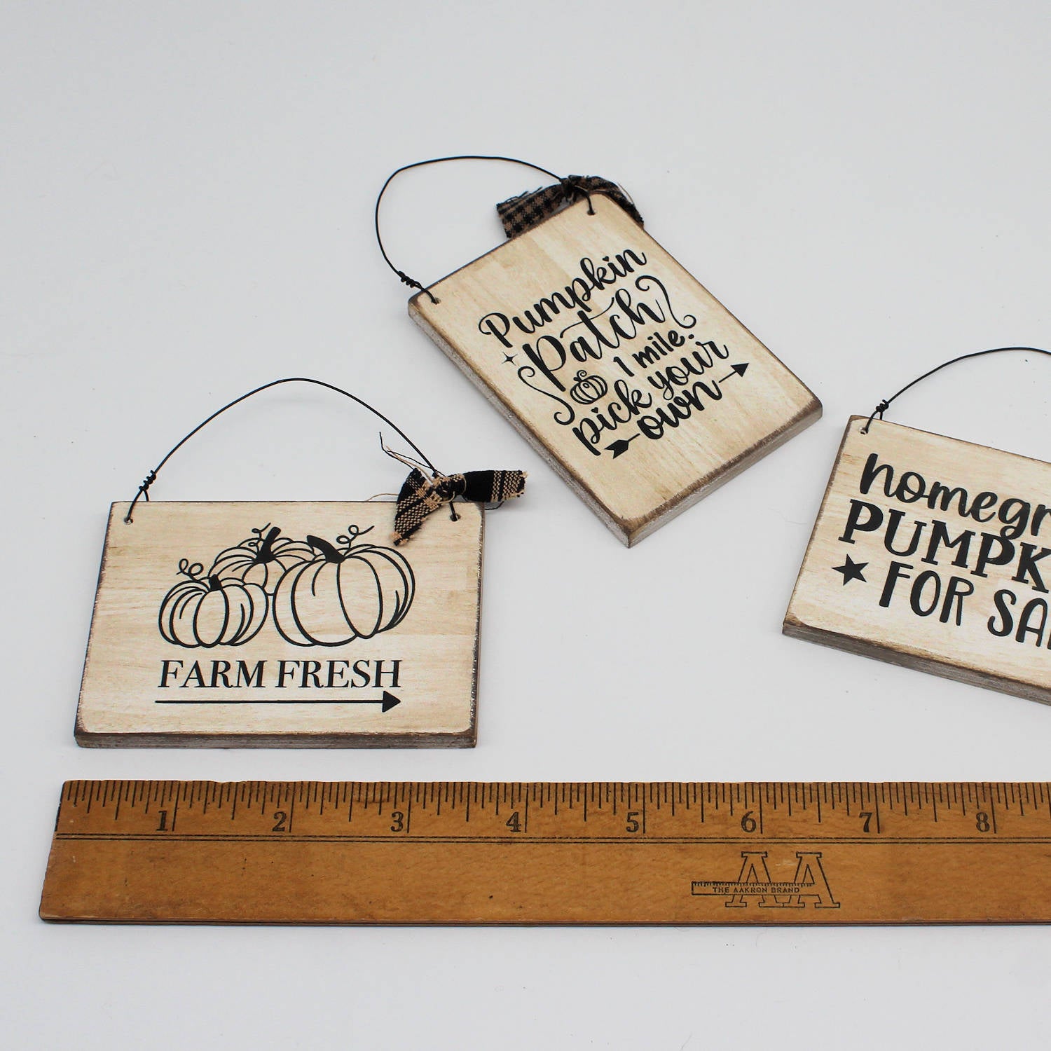 Three wooden signs with autumn-themed text and graphics, one with a ruler for scale.