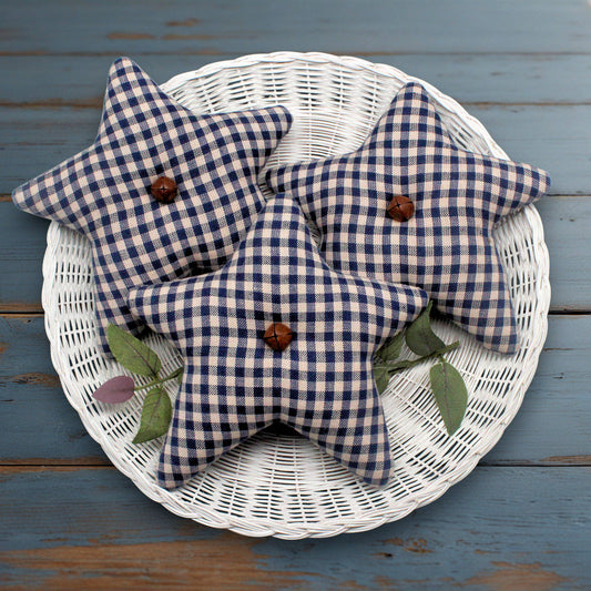 Blue and beige checkered fabric star bowl fillers with rusty bells on a white wicker basket against a blue wooden background.