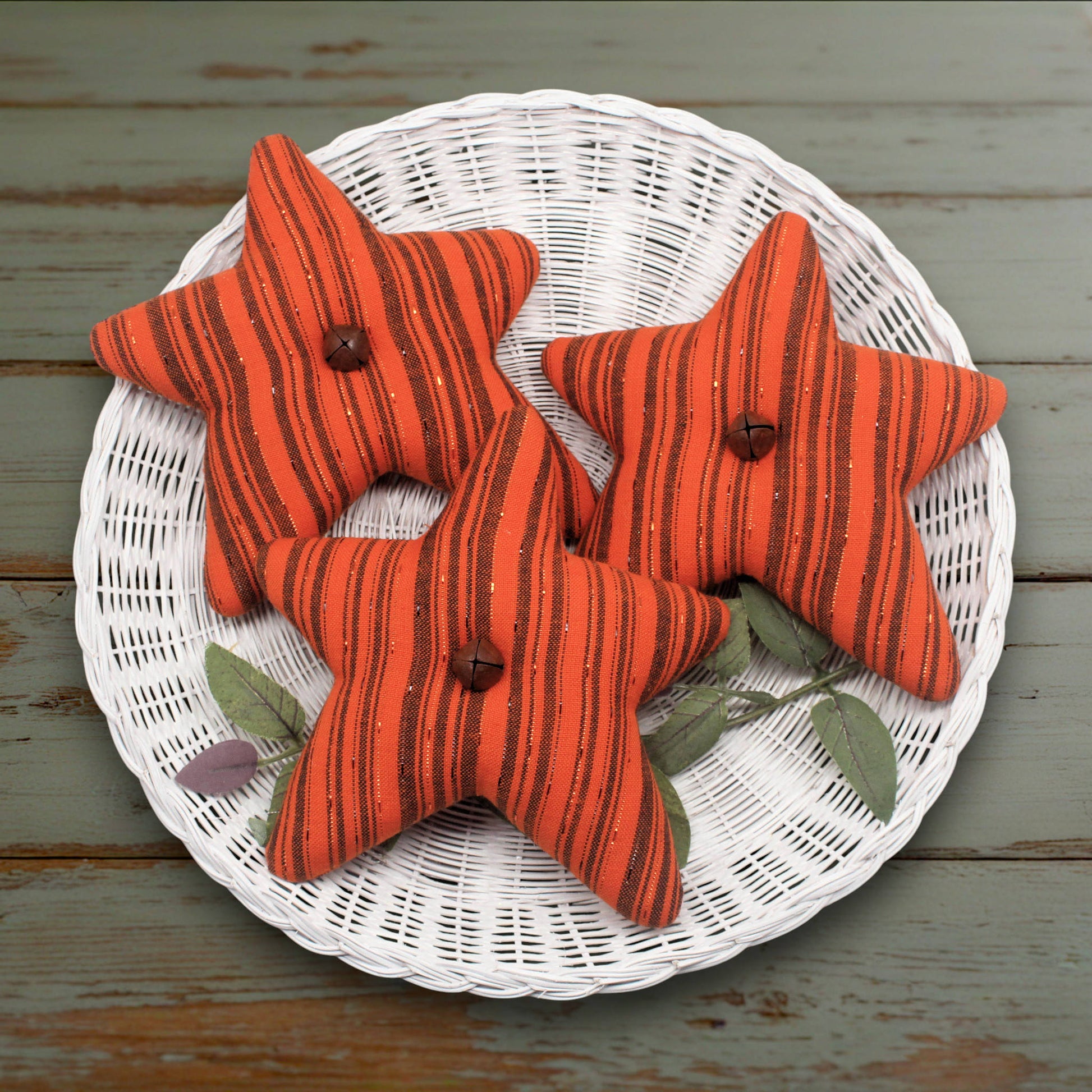 Set of three fabric stars in orange fabric with black stripes and rusty bells in the centers