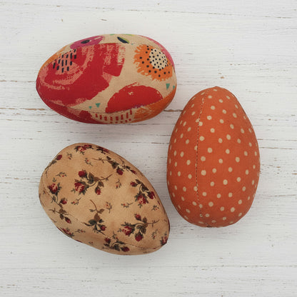 Three grungy fabric eggs with floral and polka dot patterns on a white background