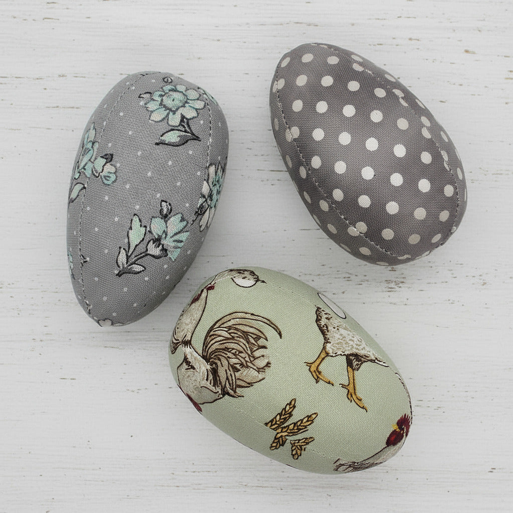 Three fabric-covered eggs with different patterns on a white background