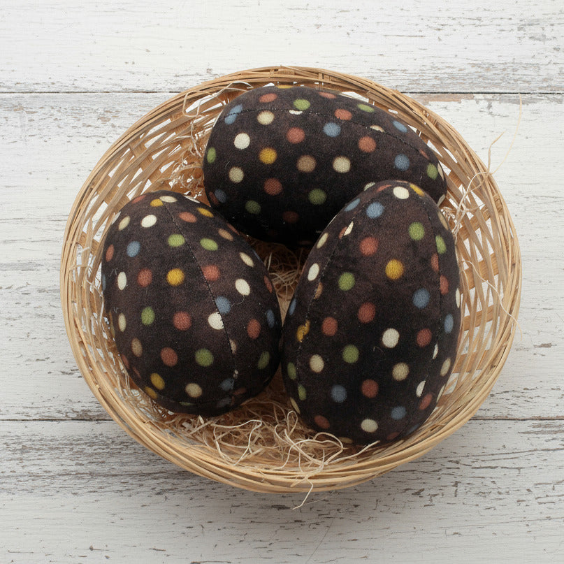 Three brown eggs with colorful polka dots in a woven basket on a white background