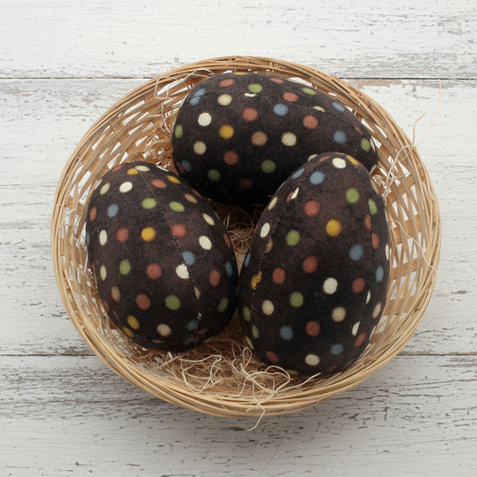 Three brown eggs with colorful polka dots in a woven basket on a white background