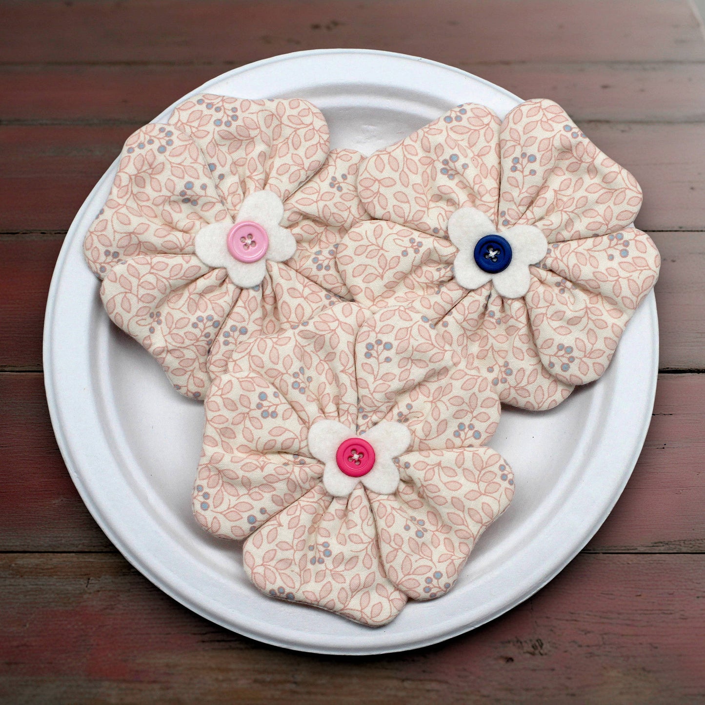 Floral-patterned fabric flowers with buttons on a white plate against a wooden background