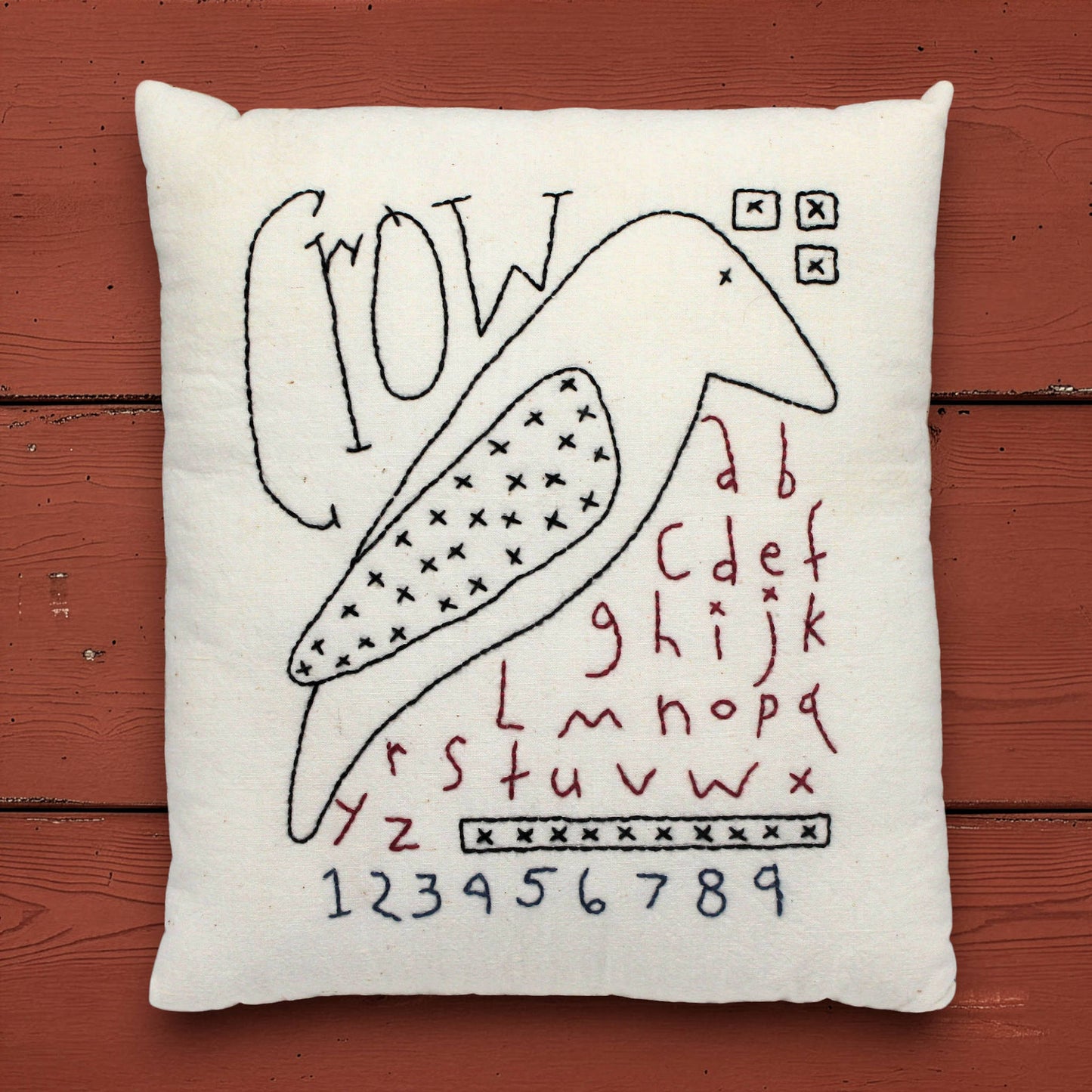 Decorative pillow with black crow and red text on a wooden surface