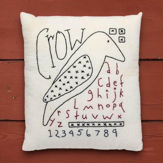 Decorative pillow with black crow and red text on a wooden surface