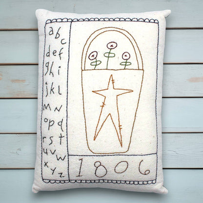 Decorative pillow with embroidered folk art design on a wooden surface