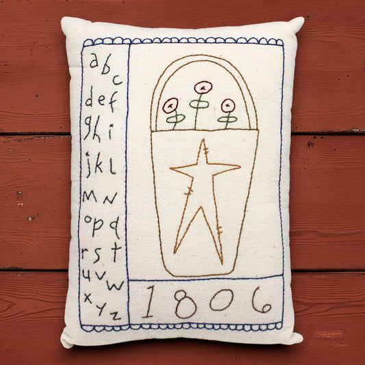 Decorative pillow with embroidered designs and text on a wooden surface