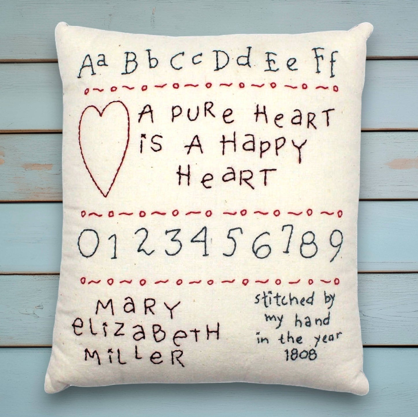 Decorative hand-stitched pillow with embroidered text and numbers on a wooden background