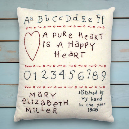 Decorative hand-stitched pillow with embroidered text and numbers on a wooden background