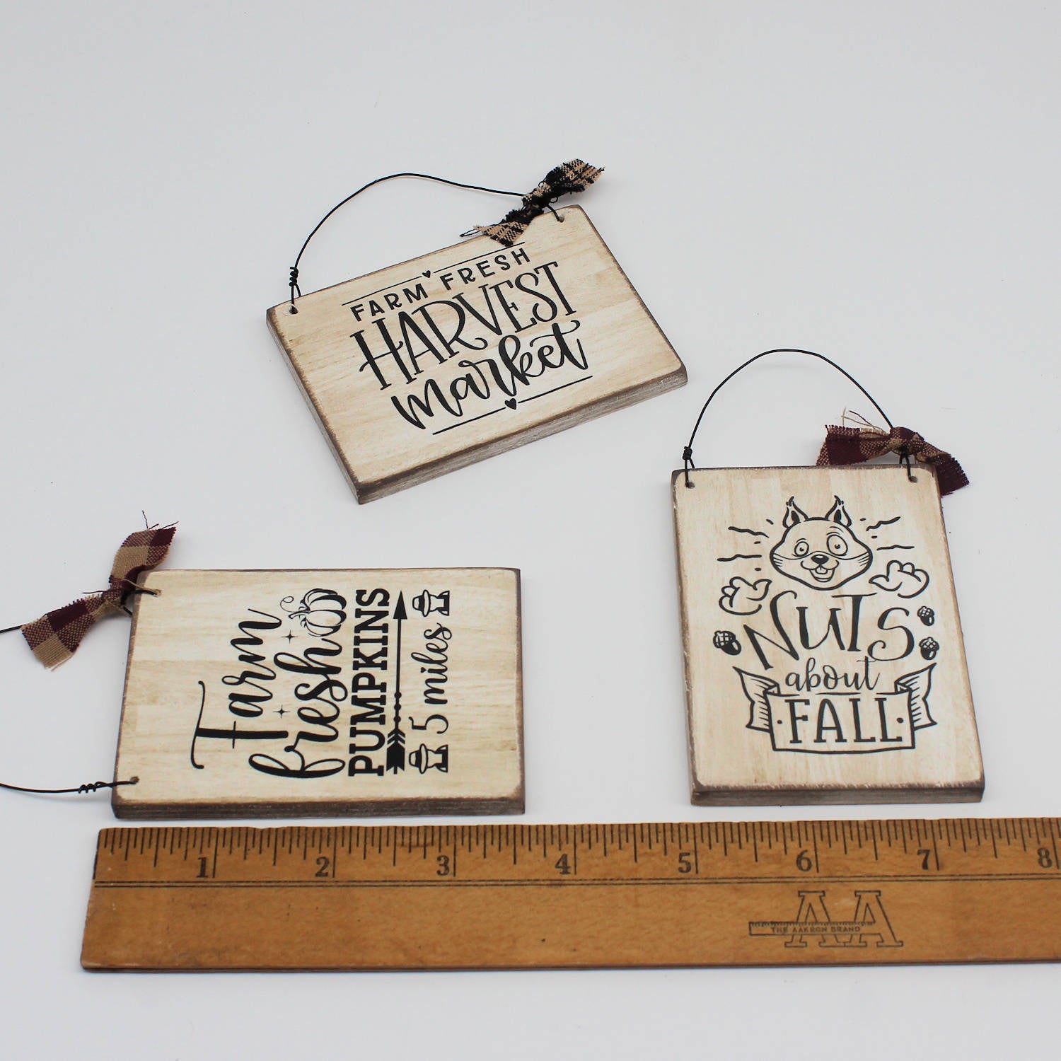 Three wooden signs with autumn-themed text on a white background, with a ruler for scale.