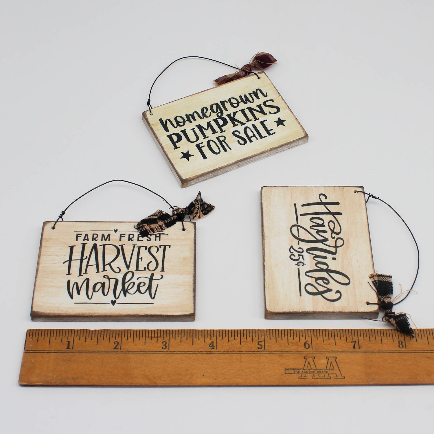 Three wooden signs with rustic text and twine hangers, shown with a ruler for scale.