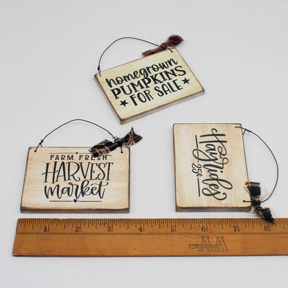 Three wooden signs with rustic text and twine hangers, shown with a ruler for scale.