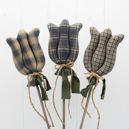 Set of three colonial blue homespun fabric tulip decorations on sticks against a white wooden background
