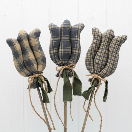Set of three colonial blue homespun fabric tulip decorations on sticks against a white wooden background