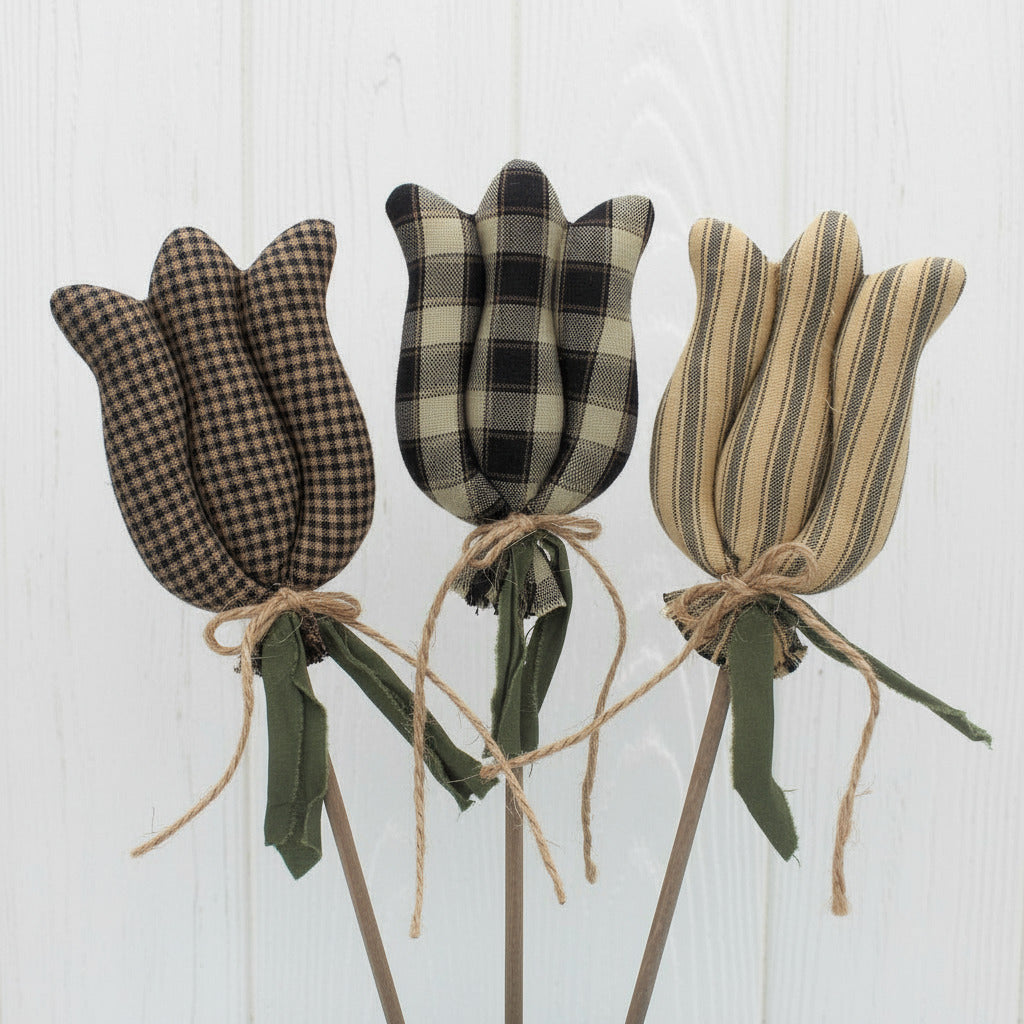 Three fabric tulips with plaid and striped patterns on sticks against a white background.