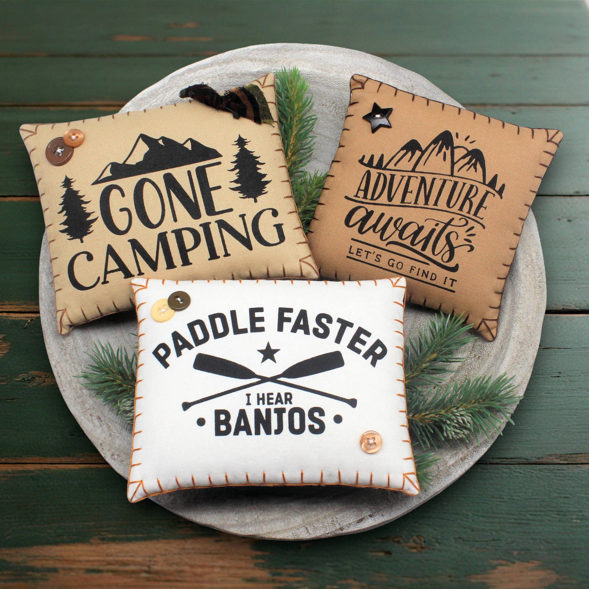 Three decorative pillows with camping-themed sayings on a wooden surface.