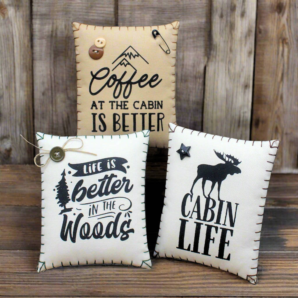 Three decorative pillows with rustic sayings on a wooden surface.
