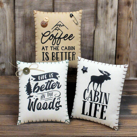 Three decorative pillows with rustic sayings on a wooden surface.