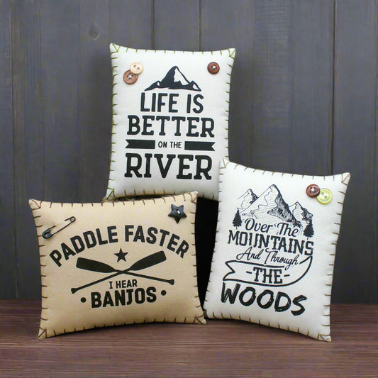 Three decorative pillows with camp quotes on a rustic wooden background.