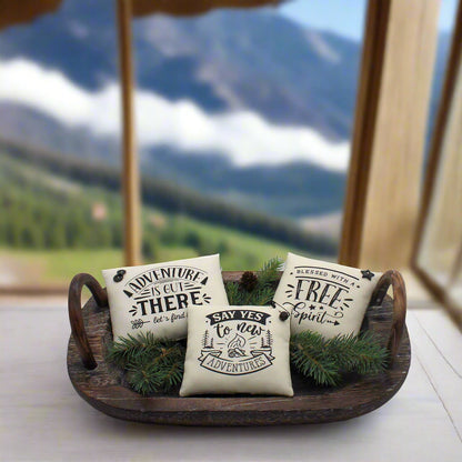 Three decorative pillows with text on a wooden tray with greenery