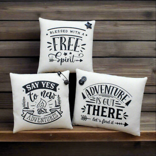 Three decorative pillows with motivational phrases on a wooden surface.