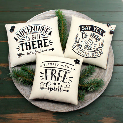 Three decorative pillows with motivational phrases on a wooden surface with greenery.