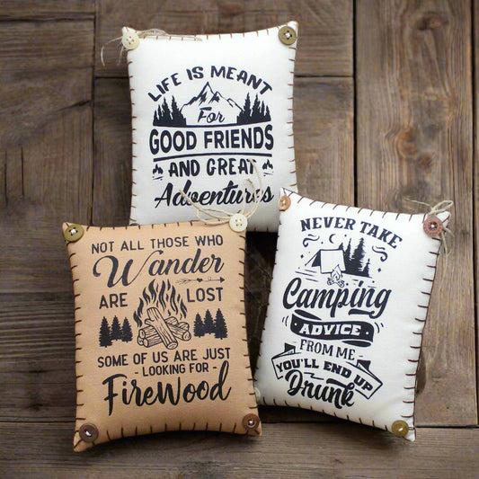 Three decorative mini pillows with humorous camping quotes on a rustic background